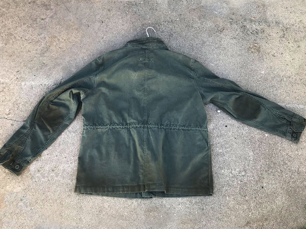 Back side of aged green cotton jacket to be worn several years by young man